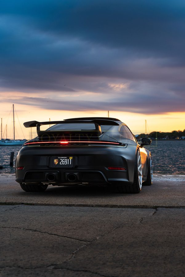 Rear three-quarter of the GT3 with marina masts and sunset