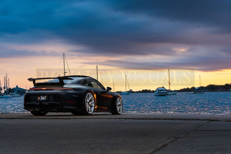 Wide rear three-quarter of the GT3 with masts of the marina and sunset
