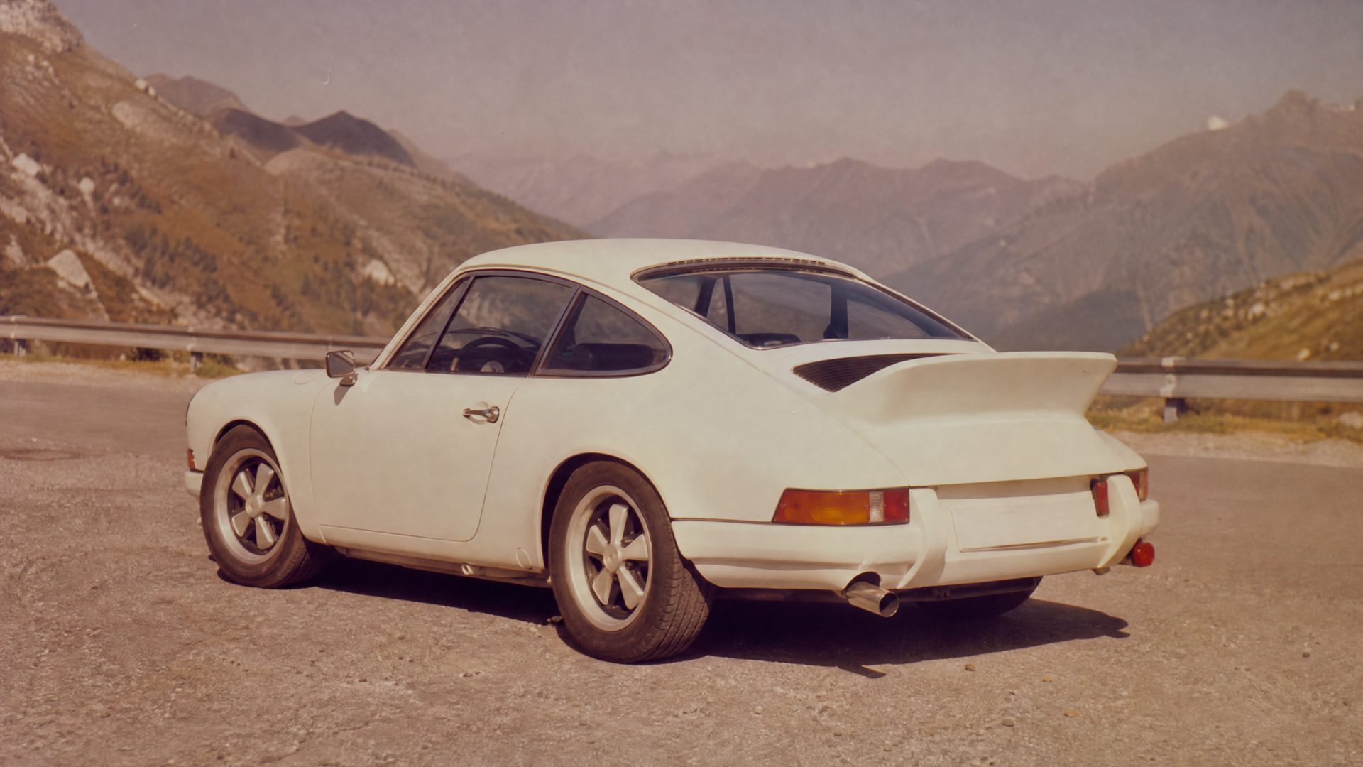 Faded 1970s colour photograph of a white 1973 Porsche 911 Carrera RS 2.7 with ducktail spoiler on an alpine road
