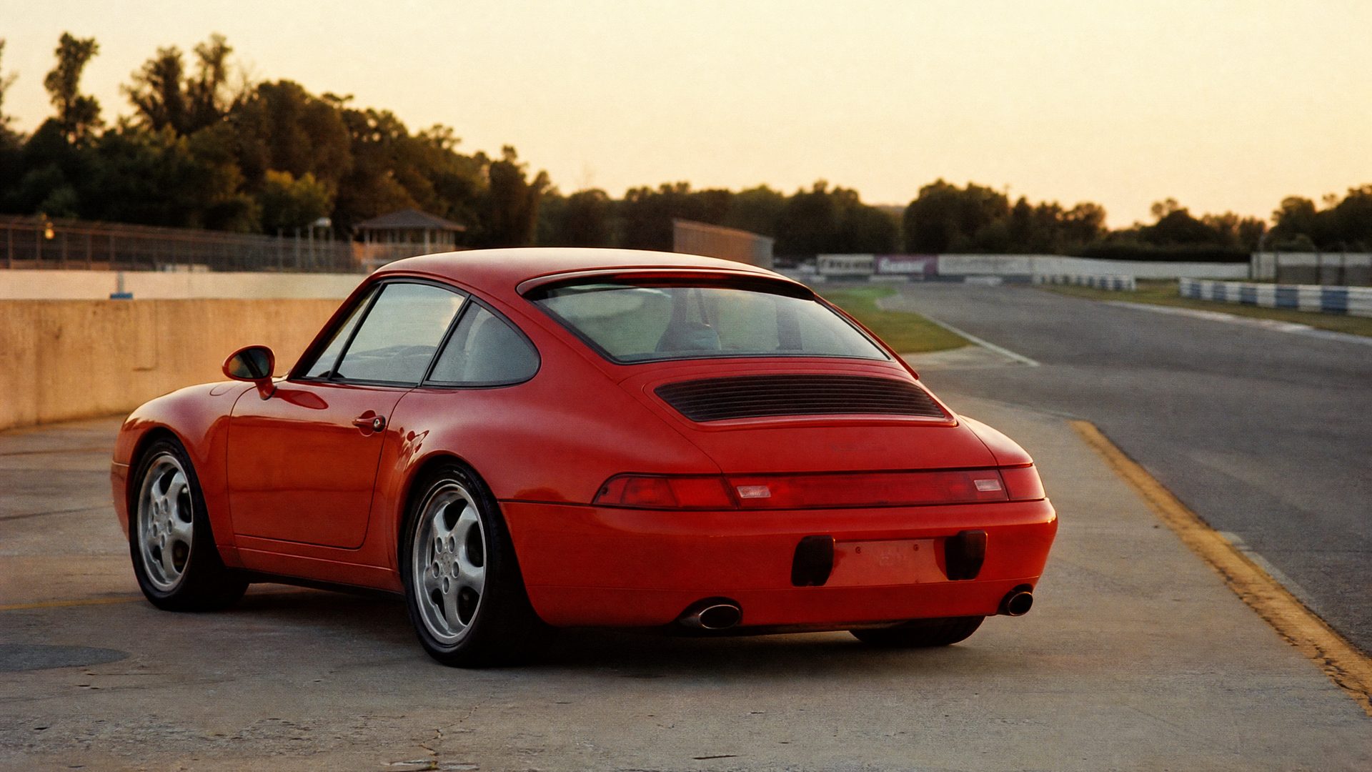 Mid-1990s photograph of a red Porsche 911 (993) at a race circuit pit exit in golden light