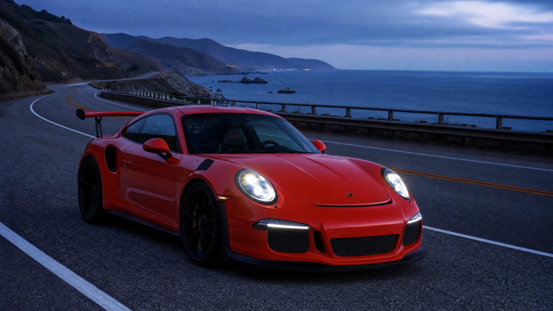 2010s photograph of a Lava orange Porsche 911 GT3 RS (991) on a coastal highway at blue hour